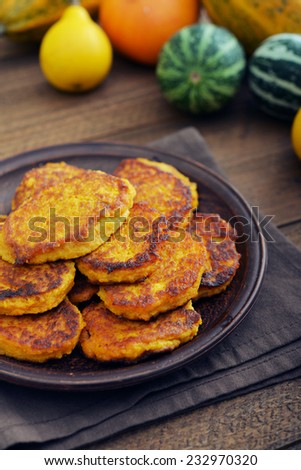 Pumpkin pancakes on plate with decorative pumpkin on wooden background