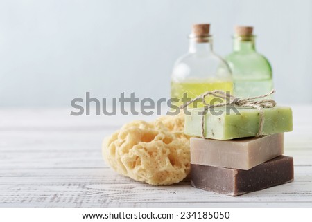 Stack of soap bars with sponge and bottles on light background