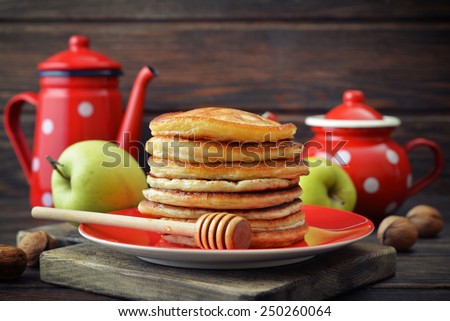 Stack of pancakes on plate with vintage teapots and fresh apples on wooden background
