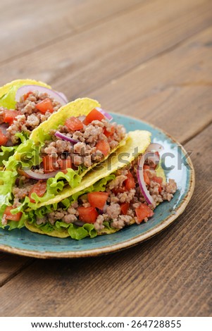 Mexican tacos with meat, onion and tomato on plate on wooden background