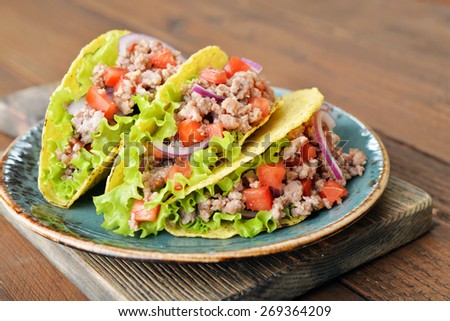 Mexican tacos with meat, onion and tomato on plate on wooden background