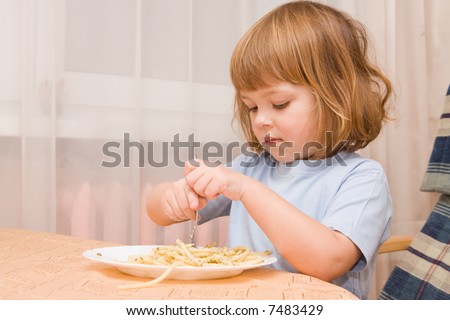 little cute girl eating spaghetti with pesto sauce