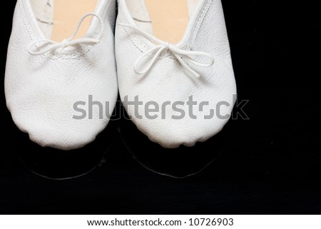 white child\'s ballet slippers on black, reflecting background