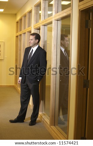 A businessman stand in the hallway of an office talking with an employee
