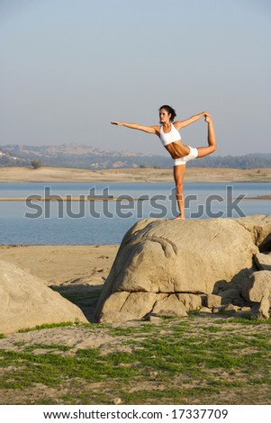 A young woman on top of a rock going yoga at sunset in a white fitness outfit