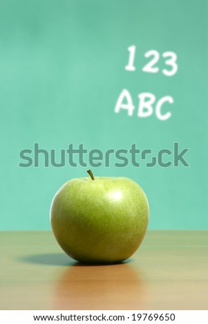 An apple on a teachers desk in the classroom with abc's