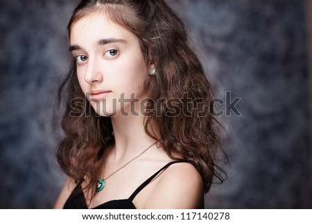 Pretty girl with long brown curly hair. Fashion studio portrait isolated against black background. Wearing black dress.