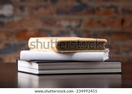 Vintage old and new books on a wooden table top  against a brick wall