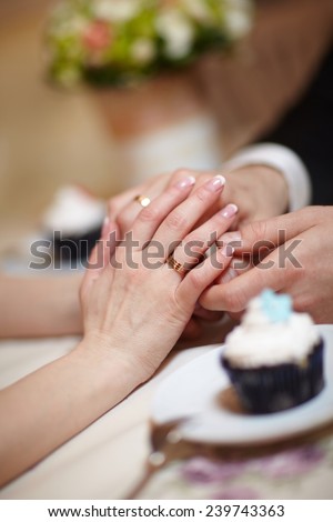 hands of a young wedding couple, bridal bouquet and sweet cake on a table