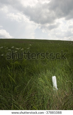 Economical light bulb on grass field, vertical photo