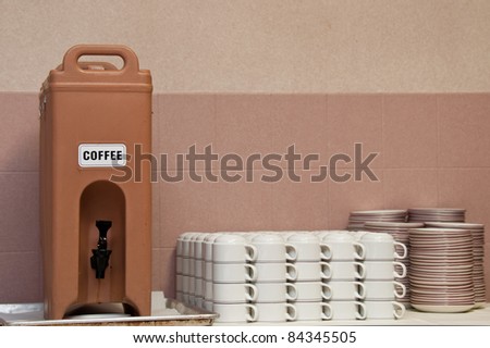 Plastic coffee dispenser sitting on a dirty drip pan. White coffee mugs and snack plates are also shown.
