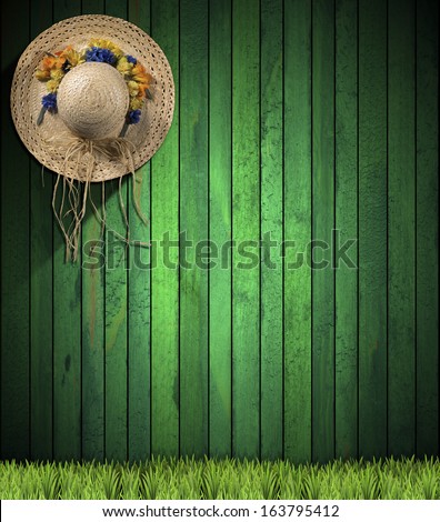 Straw Hat hanging on Green Wood Wall / Straw hat with colored flowers hanging on a green wooden wall with green grass