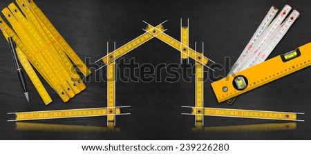 House Project - Yellow Wooden Meter. House project concept. Wooden meter ruler in the shape of house with drawing, propelling pencil, two meter tools and spirit level on a blackboard