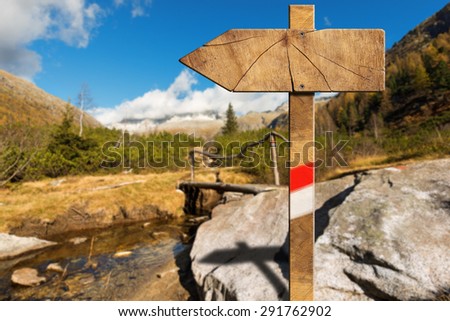 Wooden Directional Trail Sign in Mountain / Wooden trail directional sign with one empty arrow in a blurred mountain landscape