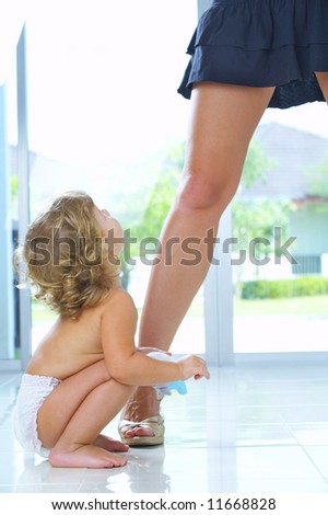 High key portrait of nice baby sitting by  mama’s leg