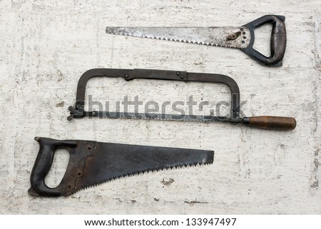 Three different used old fashioned saws in white rustic wooden background