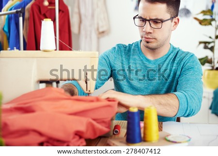 Young male fashion designer working on sewing machine