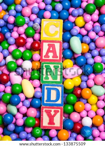 Candy spelled out in wooden toy blocks surrounded by colorful chocolates