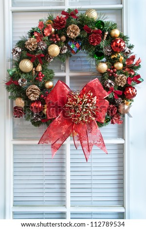 Bells, balls, shells, colored pine cones, tiny red bows  and a big red bow decorate a green Christmas wreath hanging on a door.
