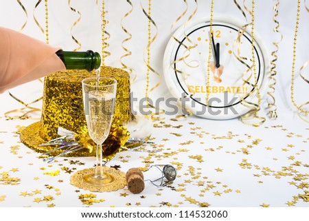 A flute of champagne and a gold glittery party hat sit in front od a clock ticking down the old year.