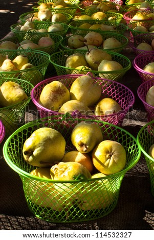 Ripe. juicy pears sit in pink or green wire baskets at a vegetable stand.