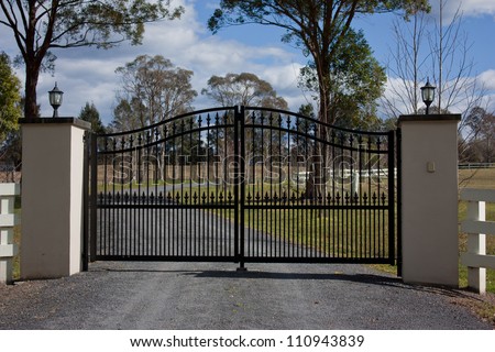 Black wrought iron entrance gates to rural property with trees and sky in background
