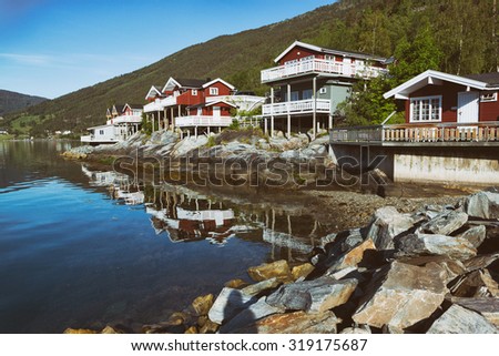 rorbuer - traditional norwegian red wooden house to stand at the lakeside and mountains in the distance, norway