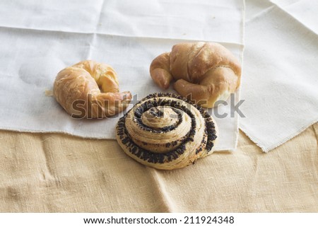 Sweet swirl pastry with poppy seeds and two croissants on the rustic textile tissues.