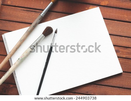 Blank paper with artist brushes on wooden planks