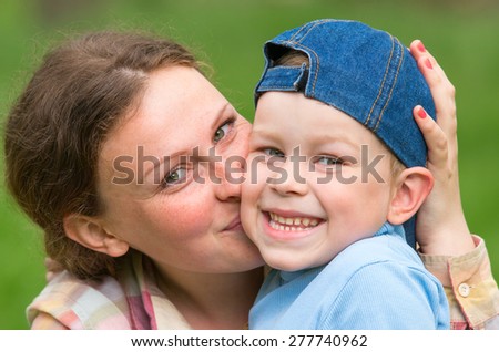Close-up, Mom kissing son on the cheek, and he is happy and smiling. Family composition