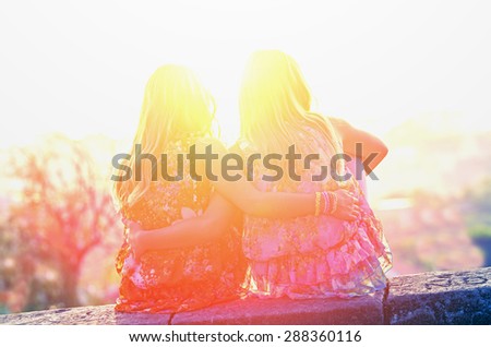 Two twin sisters sitting on the roof of embracing and looking at the sunset. Vintage Family composition