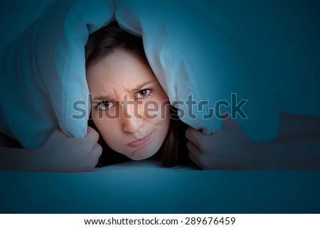 Woman with a pillow over her head, not wanting to get out of the bed in the dark