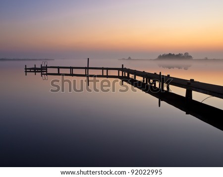 Bent jetty with mooring post during spectacular sunset over lake