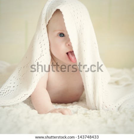 Little baby with Down syndrome hid under blanket shows tongue