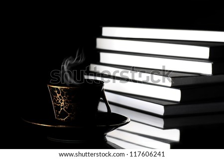 Cup or hot coffee with steam placed in front of large pile of books on black background