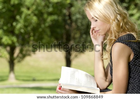 Young attractive blonde woman reading a book in park outdoor