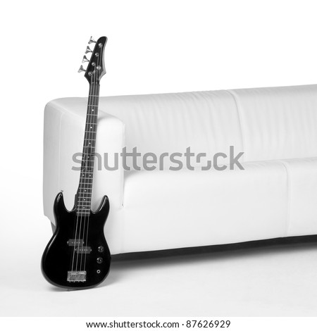 black bass guitar lean against white couch in white back