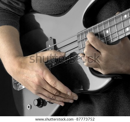 female hands on the detail of a black bass guitar in dark back
