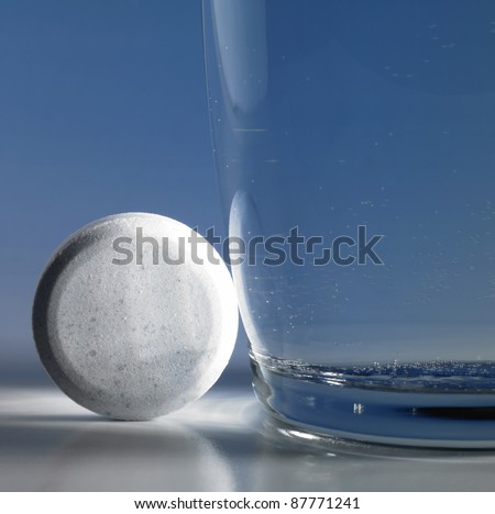 white fizzy tablet beside and a glass of water. Closeup studio shot in blue back