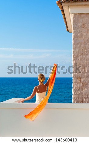 Beautiful elegant woman in white dress greeting somebody from the sea. Crete. Greece.