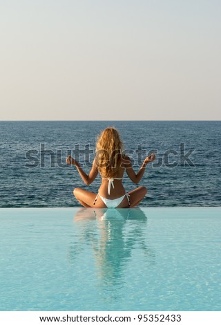 Sexy woman in yoga lotus meditation position on the edge of infinity pool. Crete. Greece