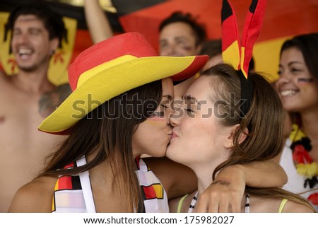 Cheerful couple of German lesbian soccer fans kissing each other celebrating victory.