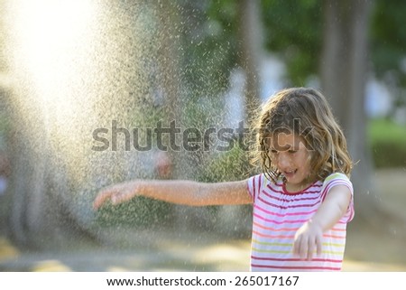 Happy smiling little girl outdoor in a sunny day enjoying the light rain.