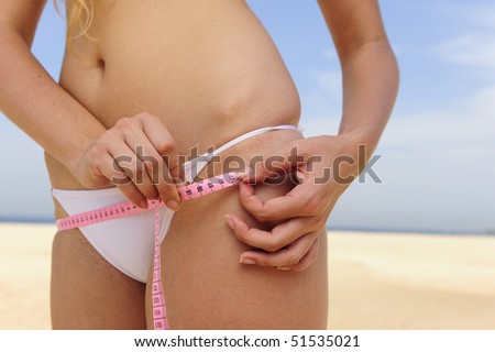 Bikini body:: Young woman wearing bikini measuring her hips on the beach