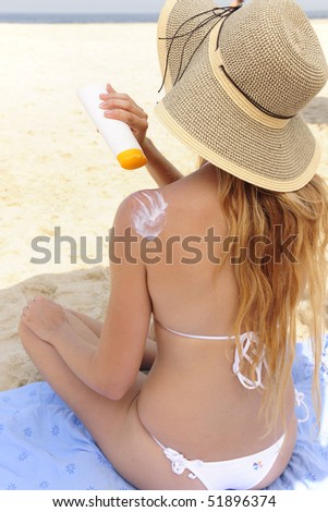 woman applying sunscreen lotion lotion at the beach, rear view