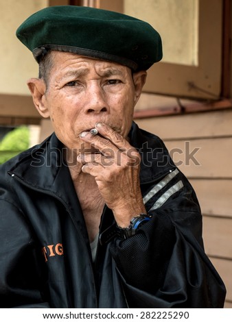 MAE TAN NOI, THAILAND - MARCH 22 2015: Elderly Thai man sits and smokes at remote train station Mae Tan Noi in Northern Thailand.