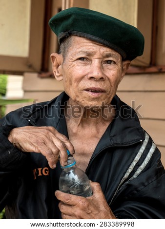 MAE TAN NOI, THAILAND - MARCH 22 2015: Elderly Thai Man, sits and smokes at remote train station Mae Tan Noi on one of the hottest recorded days in Northern Thailand.