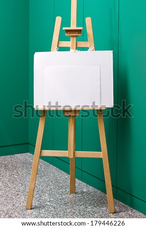 Wooden easel with blank canvas in front of a green wall