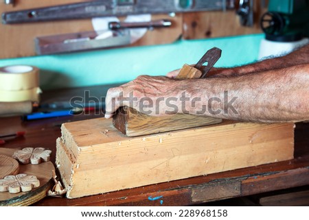 cabinetmaker hands sanding a piece of wood in his workshop with tools on the background / carpenter\'s hands working with wood
