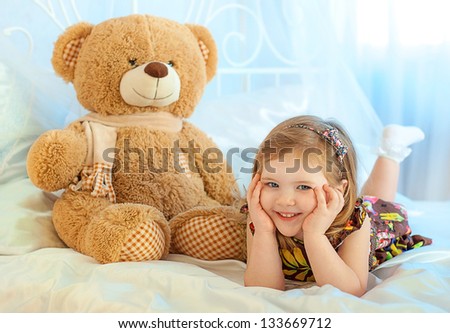 little girl lying on the bed. Teddy bear.